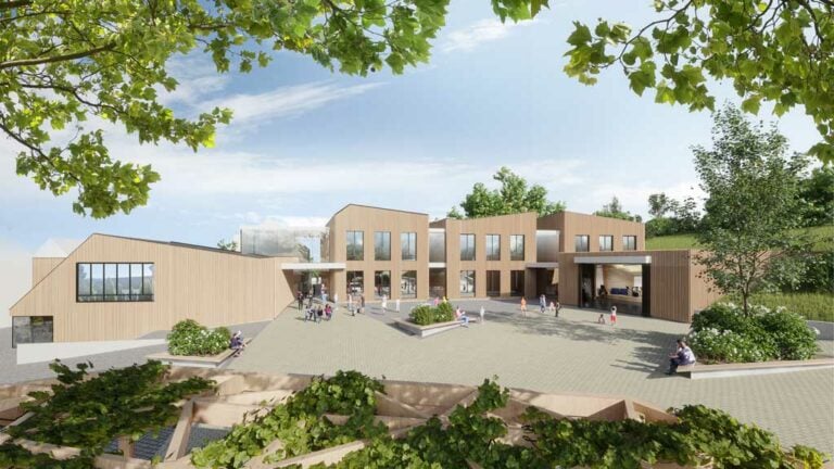 Vue de la place du village sur les cubes à façade bois de l'école et de la salle de musique du campus scolaire à Bettborn, création de BALLINIPITT architectes urbanistes.